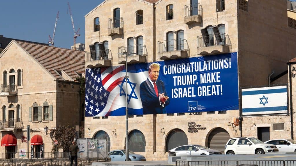 Banner de Agradecimento com a foto do presidente dos EUA e a junção das bandeiras de Israel e dos EUA. O banner está em um prédio antigo.